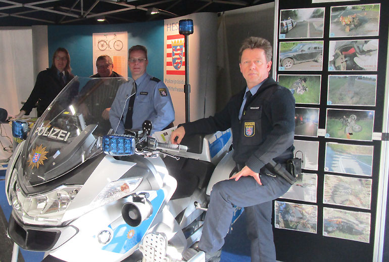 Das Polizei-Team am BOB-Infostand auf der Motorradmesse Gieißen vom Sonntag - im Hintergrund die Unfallbilder der B 276 