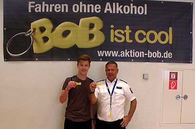 PHK Andreas Düding und eine junger Standbesucher präsentieren den BOB-Schlüsselanhänger vor dem BOB-Banner