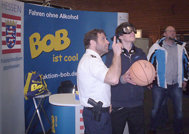 PHK Petry erläutert einem Besucher des BOB-Standes die Übung mit der Rauschbrille und dem Basketballkorb