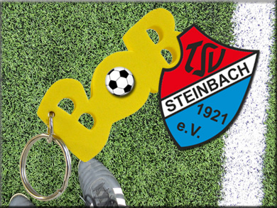 Der BOB-Schlüsselanhänger mit Ball und dem Logo des TSV Steinbach auf einem Fußballplatz	