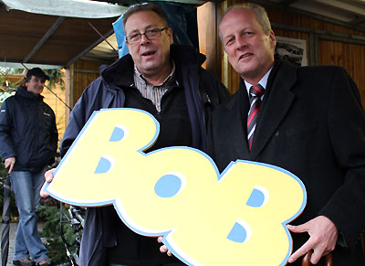 Dautphetals Bürgermeister Bernd Schmidt (rechts) mit dem Vorsitzenden Lothar Dönges und dem überdimensionalen BOB-Schriftzug, beobachtet von Frank Löber 