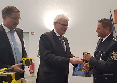 Polizeihauptkommissar Jörg Pfeiffer erhält ein Präsent von Staatssekretär Werner Koch und Polizeipräsident Bernd Paul überreicht