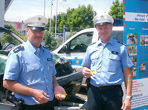 Die beiden Akteure der Polizei, POK Manfred Müller und PHK Lothar Weil, in Aktion vor dem ausgestellten Unfallauto